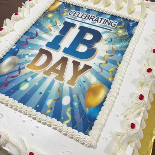 Celebration cake for IB Day 2024 with a vibrant printed design and white frosting decorations.